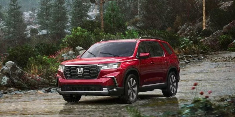 Red 2024 Honda Pilot driving in rainy weather with windshield wipers on
